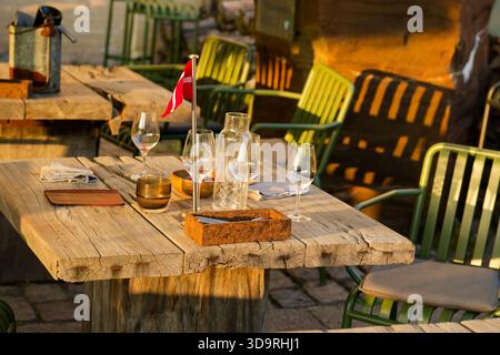 Holztisch im alten Stil mit Rissen hält kanadische Flagge Gläser Besteck Kerzenservietten und grüne Metallstühle mit Kissen in der Nähe Stockfoto