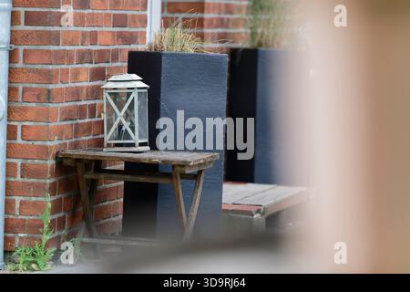 Ein rotes Backsteingebäude mit einer kleinen Einstiegsstufe ist von hohen Grasbetten eingerahmt. Neben der Tür steht ein alter Holztisch mit einer alten weißen Laterne Stockfoto
