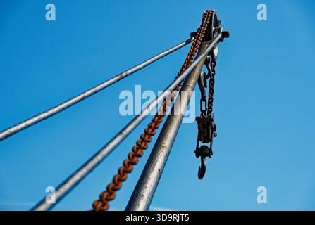 Ein alter Industriekran rammt vor einem hellblauen Himmel, mit einer dicken, rostigen Kette, die vertikal hängt und in einem starken Metallhaken in Kopenhagen endet Stockfoto