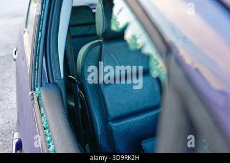 Ein lila Wagen mit einem zersplitterten Seitenfenster auf der Beifahrerseite zeigt Glassplitter, die aus den Kanten ragen. Die Innenausstattung aus schwarzem Leder Stockfoto
