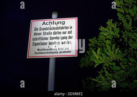 Ein deutsches Schild mit der Aufschrift Achtung warnt, dass die Einfahrten auf dieser Straße eine schriftliche Genehmigung von Eigentümern erfordern, die auf einem Metallpfosten neben Laub montiert sind Stockfoto