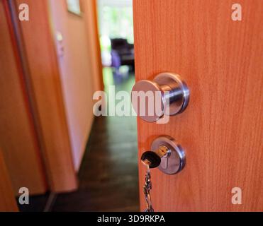 Eine braune hölzerne Hoteltür steht mit einem Schlüssel in das Schloss. Ein Teil des Innenraums ist sichtbar, einschließlich einer Wand und einem Stuhl im Hintergrund. Stockfoto
