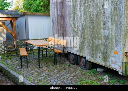 Ein müder Nutzwagen steht mit Platten Reifen und grünen Moosflecken. Daneben steht ein neuer Tisch mit Holzlatten und Metallbeinen mit Matte Stockfoto