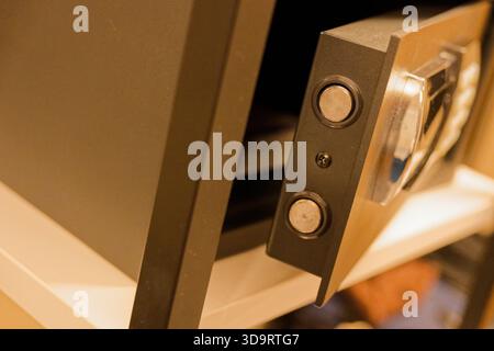 Ein kleiner Hotelsafe sitzt etwas offen auf einem Regal, die dunkle Tastatur und die dicke Tür zeigen robustes Metall, während die Lücke auf eine kürzliche Nutzung und einen bescheidenen Abschlussball hindeutet Stockfoto