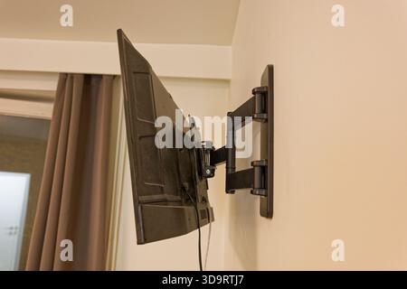 Moderner Flachbildfernseher, der an einem verstellbaren Wandarm in einem gemütlichen, modernen Wohnzimmer befestigt ist. Perfekt für Design, Wohnkultur und Technologie Stockfoto
