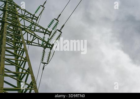 Ein hoher Power Tower steht unter einem flachen grauen Himmel und hält dicke elektrische Kabel, die nach außen reichen. Der Stahlrahmen fühlt sich kalt streng und funktionell an Stockfoto