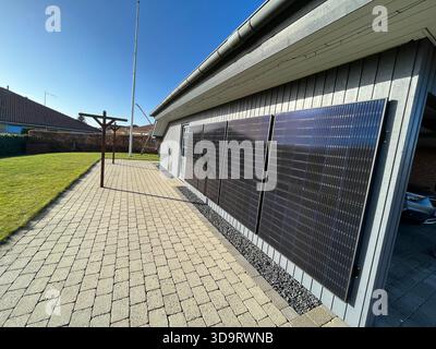 Ein modernes Haus mit Sonnenkollektoren an der Seitenwand. Die Gegend verfügt über eine gepflasterte Terrasse mit einer Wäscheleine und einem gepflegten Rasen. Solarstrom Stockfoto