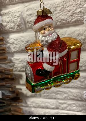 Ein festliches Weihnachtsschmuck mit einem fröhlichen Weihnachtsmann, der auf einem bunten Zug sitzt. Das Ornament ist glänzend und mit Glitzer verziert Stockfoto
