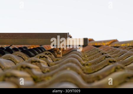 Nahaufnahme eines Solarmoduls auf einem gekachelten Dach, das die Textur der Fliesen und der Befestigungsteile zeigt. Stockfoto