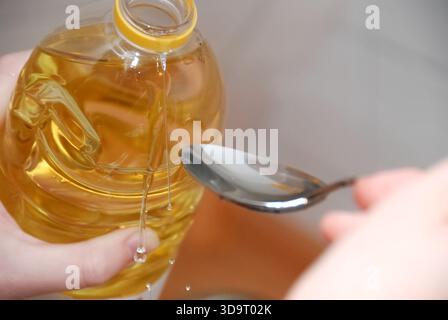 Eine Person, die Flüssigkeit aus einer Flasche in einen Löffel gießt und den Ölfluss zeigt. Der Hintergrund ist verschwommen und konzentriert sich auf die Wirkung des Gießens. Stockfoto