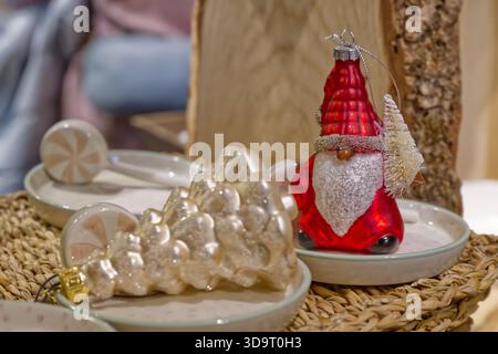 Eine festliche Ausstellung mit einem roten Weihnachtsmann-Ornament neben einem silbernen Weihnachtsbaum-Ornament auf dekorativen Tellern. Der Hintergrund ist leicht verschwommen Stockfoto