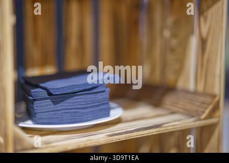 Ein Stapel dunkelblauer Servietten auf einem weißen Teller auf einem Holzregal. Stockfoto