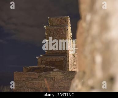 Eine Steinmauer in der Nacht, teilweise beleuchtet, mit einem dunklen Himmel im Hintergrund. Die Wand besteht aus gestapelten Steinen, die eine rustikale und eine bilden Stockfoto