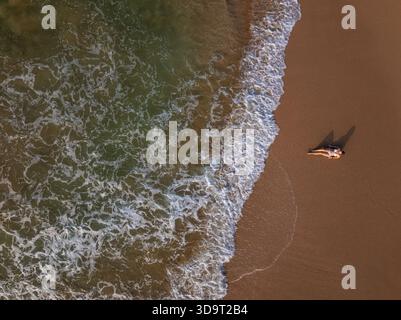 Topdown-Ansicht der jungen Frau, die an der Küste liegt, während Wellen über sie am Talalla Beach, Sri Lanka, strömen Stockfoto