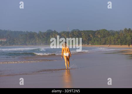 Junge Frau in der Schwimmsuite läuft entlang der Küste am Talalla Beach, Sri Lanka Stockfoto