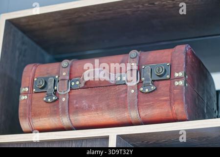 Ein Vintage-Holzkoffer mit Lederriemen und Metallverschlüssen auf einem Regal. Der Koffer hat eine satte rötlich-braune Farbe und ein klassisches Design, e Stockfoto