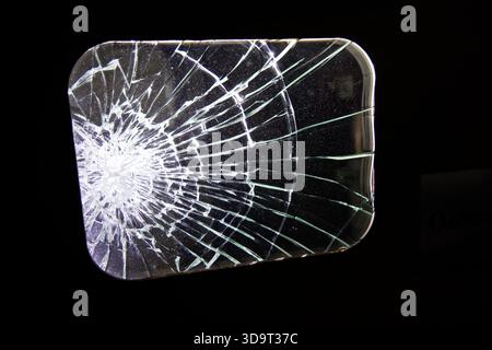 Nahaufnahme einer zersplitterten Glasscheibe mit komplexen Rissen, die von der Mitte ausstrahlen, vor schwarzem Hintergrund. Stockfoto