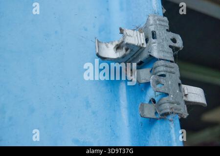 Nahaufnahme eines rostigen Metallscharniers auf blauer Oberfläche, zeigt Verschleiß und Spinnweben, was auf Vernachlässigung oder Alter hinweist. Stockfoto