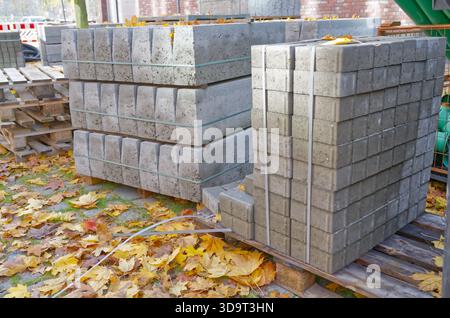 Betonblöcke auf Holzpaletten, umgeben von Herbstlaub. Die Blöcke sind ordentlich angeordnet und zeigen ihre rechteckige Form und Stockfoto