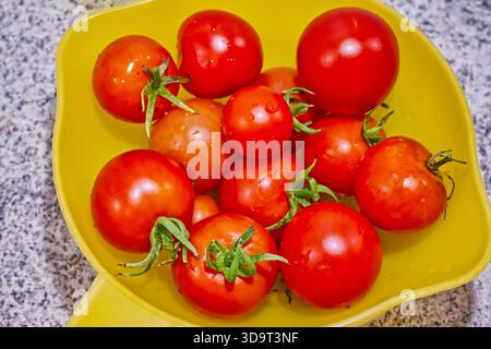 Eine Sammlung frischer, reifer Tomaten in einer mit Wasser gefüllten gelben Schüssel auf einer Granitplatte. Stockfoto