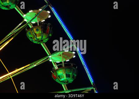 Nächtliche Nahaufnahme eines bunten Riesenrads mit beleuchteten Gondeln und leuchtenden Lichtern vor dunklem Himmel. Stockfoto