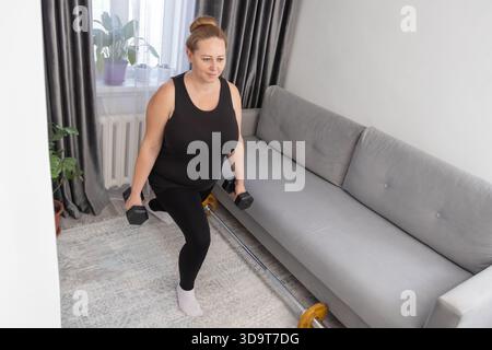 Eine Frau mittleren Alters, die während eines Fitness-Workouts zu Hause eine Kurzhantel-Ausfallschritte macht. Für die Illustration von Gesundheitsartikeln, Workout-Leitfäden und Wellness-Routinen. Stockfoto