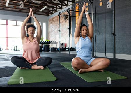 Afroamerikanische Freunde, die Lotus üben, posieren auf grünen Matten im Fitnessstudio mit Gewichten Stockfoto