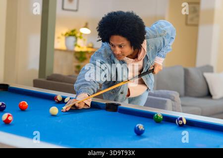 Ein Afroamerikaner lehnt sich zu Hause über den Billardtisch und hält sich zwischen Billardbällen auf Stockfoto