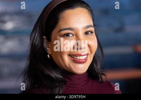 Lächelnde Frau mittleren Alters mit burgunderfarbenem Pullover und braunem Stirnband posiert im Porträtstudio Stockfoto