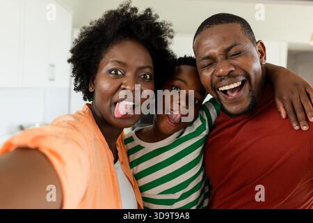Afroamerikanische Familie, die Selfie in der Küche macht, mit dem Smartphone und den Zungen ausstreckt Stockfoto