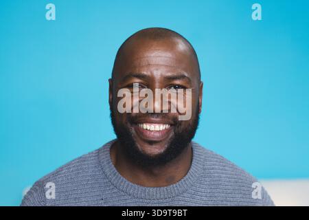 Ranghoher Afroamerikaner lächelt im Studio und trägt einen grauen Strickpullover vor blauem Hintergrund Stockfoto