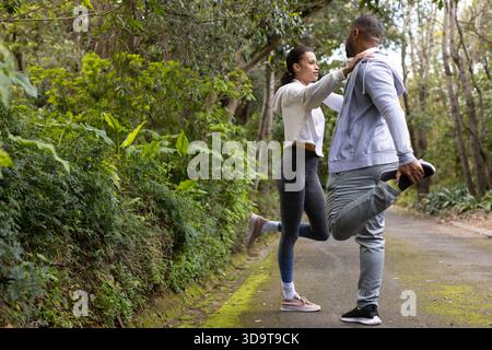 Verschiedene Paar dehnen Quadrizeps auf bewaldeten Parkwegen mit Laufschuhen, Kopierraum Stockfoto