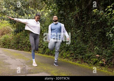Verschiedene Trainingspartner halten die Knöchel auf bewaldeten Trails mit Kopfhörern und Sneakers Stockfoto