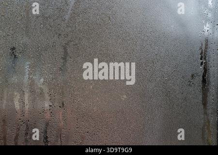 Nahaufnahme von Wassertröpfchen am nassen Fenster. Winzige Kondenswasserperlen haften an der kühlen Glasoberfläche, einige verschmelzen zu gewundenen Rillen. Kondensation ein Stockfoto