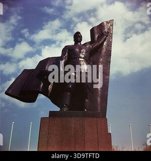 Ein Vintage-Farbfoto im Archivformat, das das riesige Kriegsdenkmal in Slowiansk, Donezk, Ukraine, während der 1980er Jahre festgehalten hat Die dunkle Metallskulptur zeigt einen sowjetischen Soldaten, der ein Maschinengewehr und ein Banner vor einem blauen Himmel hält. Diese dramatische, aus einem tiefen Winkel gezogene Aufnahme im Lenin Park (heute Silkovichny Park) unterstreicht den heldenhaften Stil des sozialistischen Realismus. Das Denkmal steht als mächtiges Symbol der Erinnerung an den Zweiten Weltkrieg und der Geschichte in der sonnigen Atmosphäre eines friedlichen Donbas. Stockfoto
