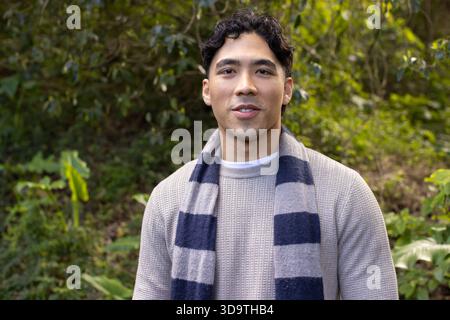 Asiatischer Mann, der in bewölktem Himmel in Strickpullover und gestreiftem Schal steht Stockfoto