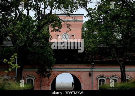 Das Torhaus des Uhrenturms, eingerahmt von Bäumen in der Meeresfestung Suomenlinna, Helsinki, Finnland, mit einem bogenförmigen Durchgang und feuchten historischen Stein- und Ziegelmauern. Stockfoto