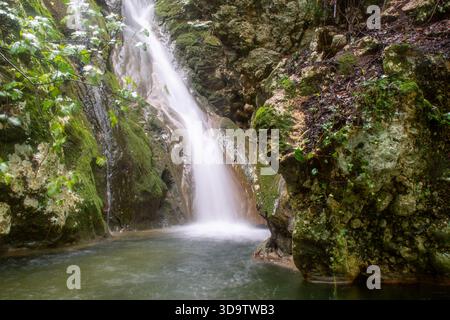 Atemberaubender Wasserfall versteckt in den felsigen Bergen von Kyprianades Korfu Griechenland, seidiges Wasser fließt über moosbedeckte Steine in einem ruhigen grünen Wald en Stockfoto