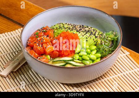 Poke Bowl mit Lachs, Avocado, Edamame Bohnen auf hölzernem Hintergrund. Trendige gesunde Meeresfrüchte Platte. Auf dem Restauranttisch. Stockfoto