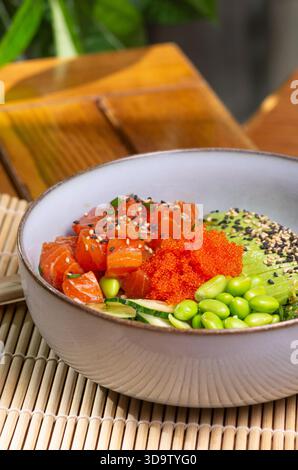 Poke Bowl mit Lachs, Avocado, Edamame Bohnen auf hölzernem Hintergrund. Trendige gesunde Meeresfrüchte Platte. Auf dem Restauranttisch. Stockfoto