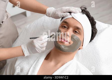 Kosmetikerin, die im Schönheitssalon Tonmaske auf das Gesicht des Mannes aufträgt Stockfoto