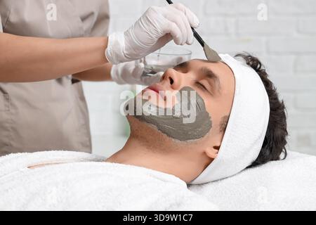 Kosmetikerin, die Tonmaske auf das Gesicht des Mannes im Schönheitssalon aufträgt, Nahaufnahme Stockfoto