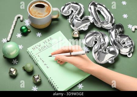 Frau mit Figur 2026, Tasse Kaffee und Weihnachtsdekor, die To-do-Liste auf grünem Hintergrund schreibt Stockfoto