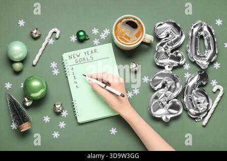 Frau mit Figur 2026, Tasse Kaffee und Weihnachtsdekor, die To-do-Liste auf grünem Hintergrund schreibt Stockfoto