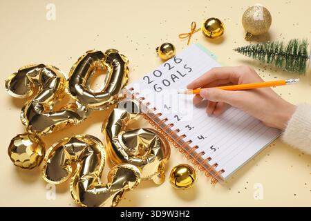 Frau mit Figur 2026 und Weihnachtsdekor, die To-do-Liste auf gelbem Hintergrund schreibt Stockfoto