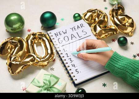 Frau mit Figur 2026, Geschenkbox und Weihnachtsdekor, die To-do-Liste auf weißem Hintergrund schreibt Stockfoto