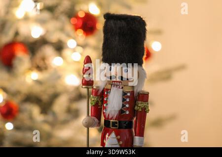 Weihnachtsnussknacker-Wache neben einem hell erleuchteten Weihnachtsbaum mit roten Ornamenten. Stockfoto