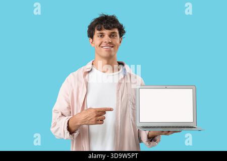 Männlicher Programmierer zeigt auf leeren Laptop auf blauem Hintergrund Stockfoto