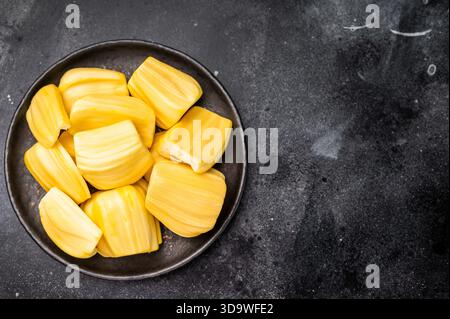 Süße, goldgelbe Jackfruchengruten (Zwiebeln), serviert auf einem schwarzen Teller auf dunklem Steinhintergrund. Exotische tropische Früchte mit Kopierraum. Stockfoto