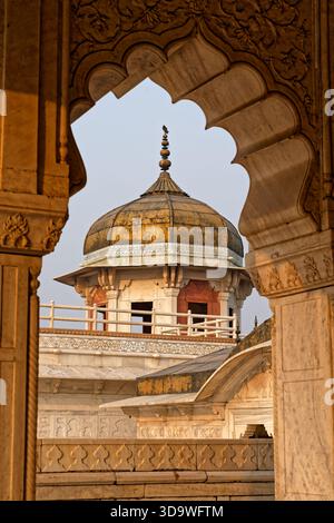 Ein Kuppelturm von Agras Rotem Fort, der zur goldenen Stunde durch einen kunstvollen Bogen gesehen wird, mit einem Vogel, der im warmen Abendlicht auf dem Gipfel thront. Stockfoto